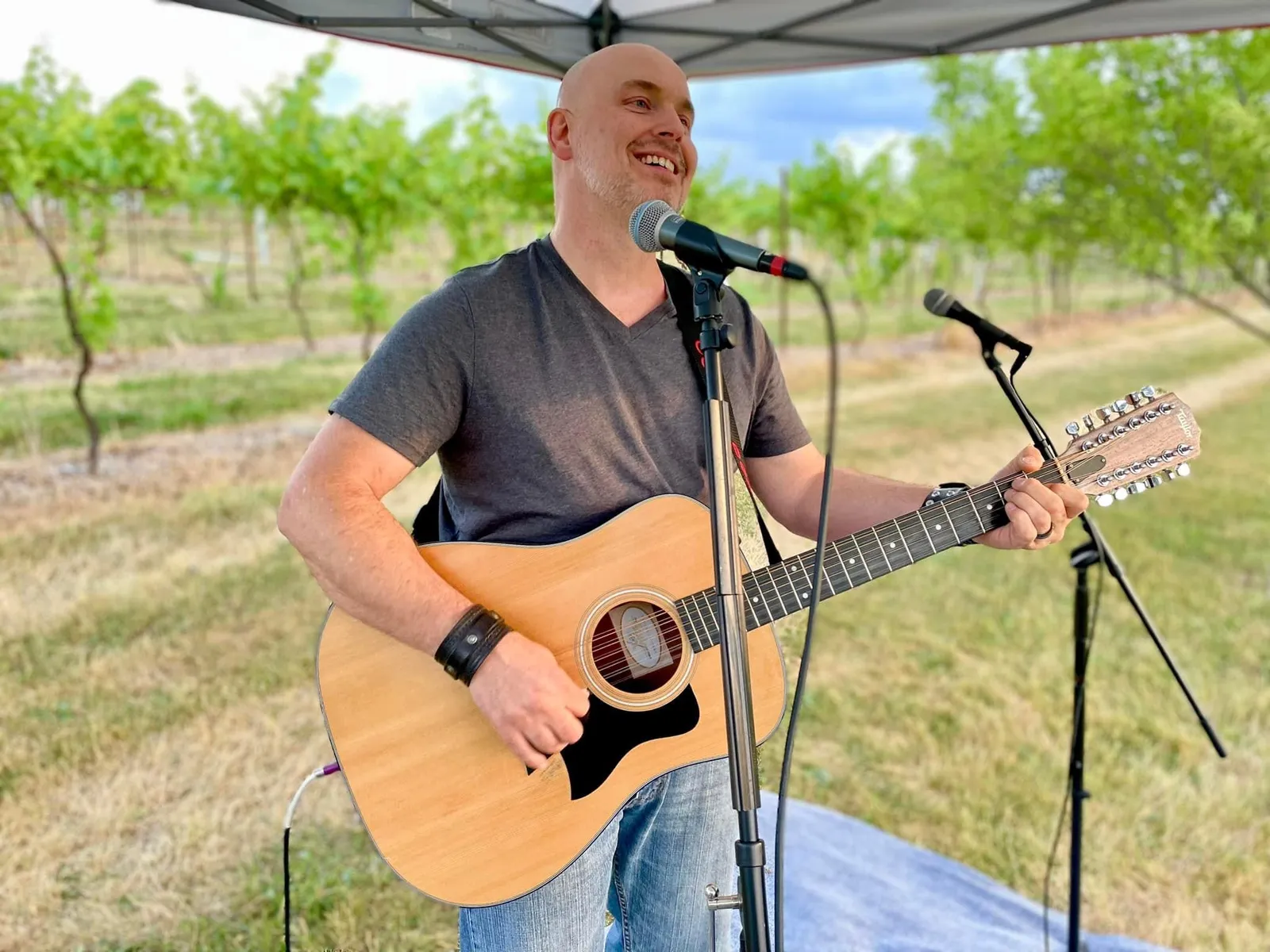 Musician Colby Dove singing and playing guitar with vineyard background.