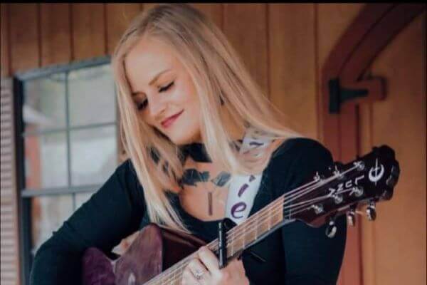 Dezzie Renae holding guitar while smiling and looking down.