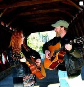 Musicians, Neil and Shannon each playing guitar while looking at each other.